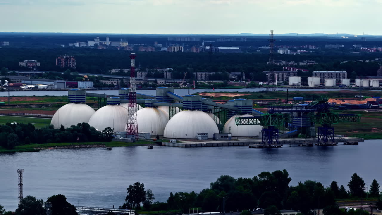 A scenic view shows the Riga Fertilizer Terminal, a key industrial and logistics hub on the Daugava River in Latvia, with its massive white dome tanks for storing chemical fertilizers for export