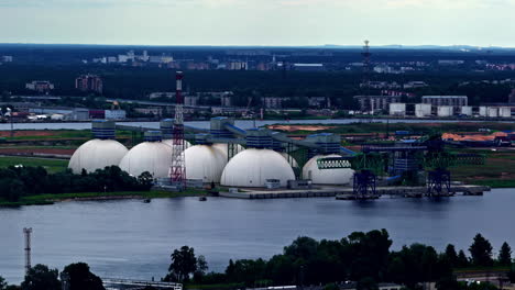 a scenic view shows the riga fertilizer terminal, a key industrial and logistics hub on the daugava river in latvia, with its massive white dome tanks for storing chemical fertilizers for export