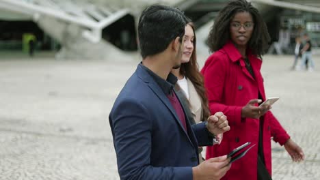 Three-young-people-walking-along-street,-talking-with-each-other