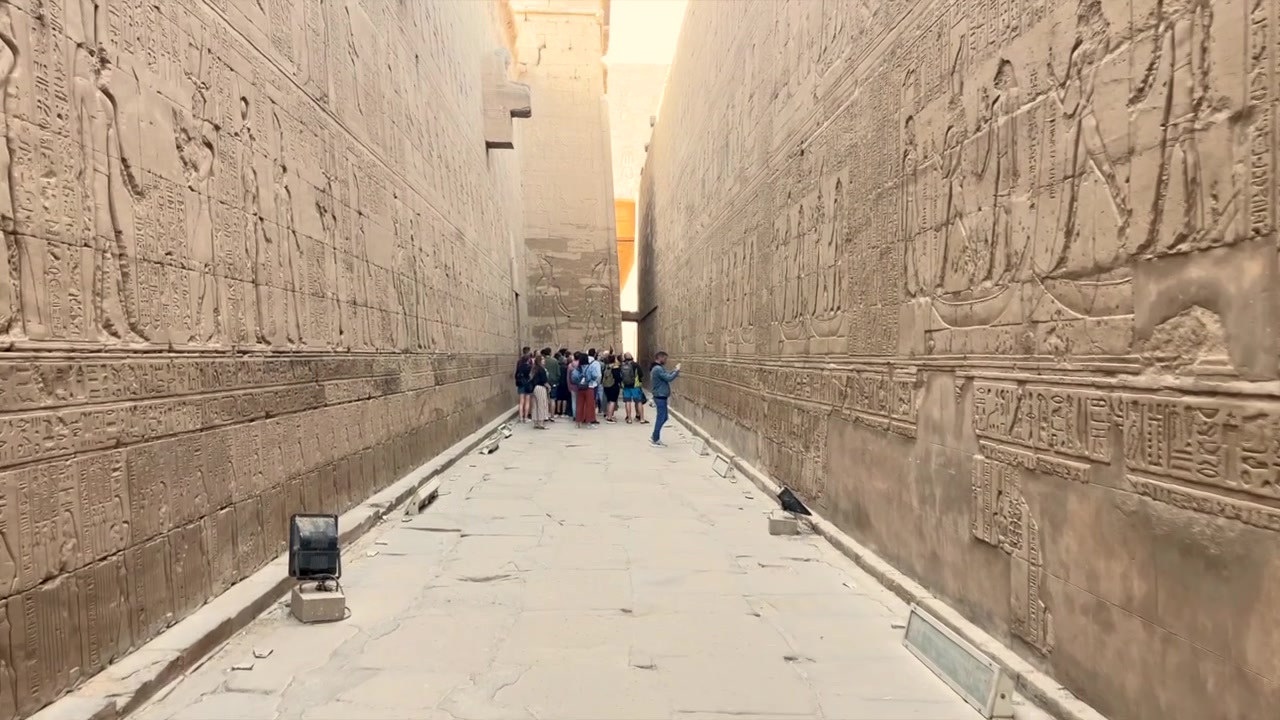 Turisti tra mura piene di geroglifici all'interno del Tempio di Horus a Edfu, Egitto. Viaggiatori che visitano un antico tempio egizio osservando i geroglifici. Telecamera in movimento verso un gruppo di turisti.