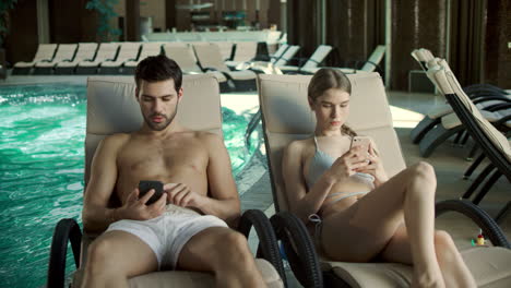 Pareja-Joven-Viendo-El-Móvil-Cerca-De-La-Piscina.-Hermosa-Familia-Relajándose-Con-Teléfonos