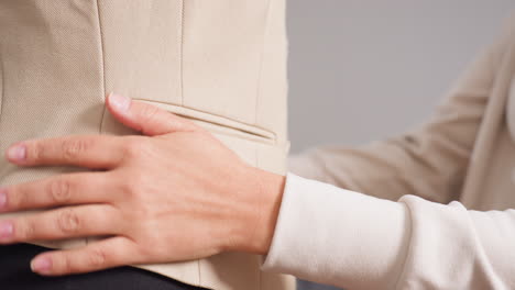 side view garment maker presses palm against beige blazer on black mannequin, straightening side seam, flattening fabric panels, ensuring precise alignment during careful tailoring