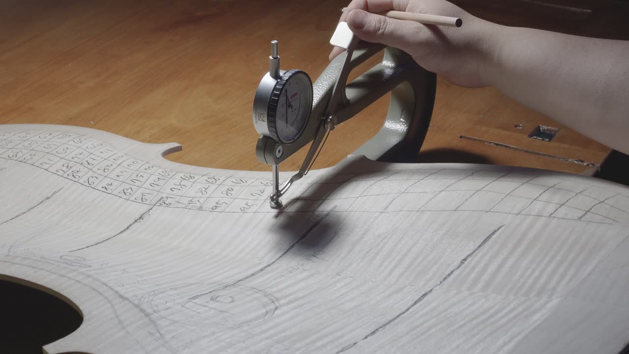 Strengeinstrumentmager, mesterluthier, udfører gradueringarbejde på celloens bagplade, bruger tykkelsesmåler, måler niveauer, bruger blyant til at skrive værdier på træ, værksted i Cremona, Italien