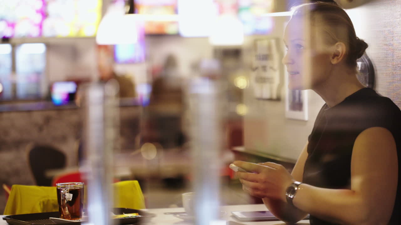 una mujer joven en un café pensando en los mensajes de texto y escribiéndolos