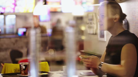 una mujer joven en un café pensando en los mensajes de texto y escribiéndolos