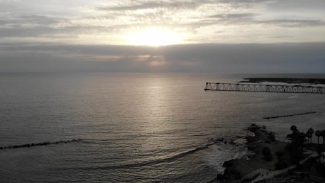 Aerial-pan-across-a-silhouette-of-a-construction-crane-on-the-coast-of-Cyprus-at-sunset-from-left-to-right