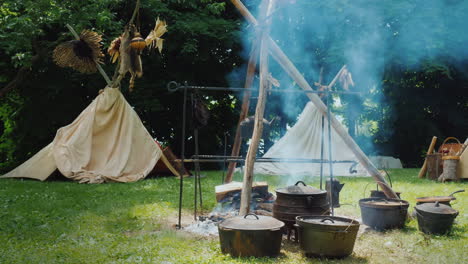 Indianercamp-Im-Wald-Essen-Wird-In-Den-Traditionellen-Wigwam-Zelten-Im-Vordergrund-Zubereitet