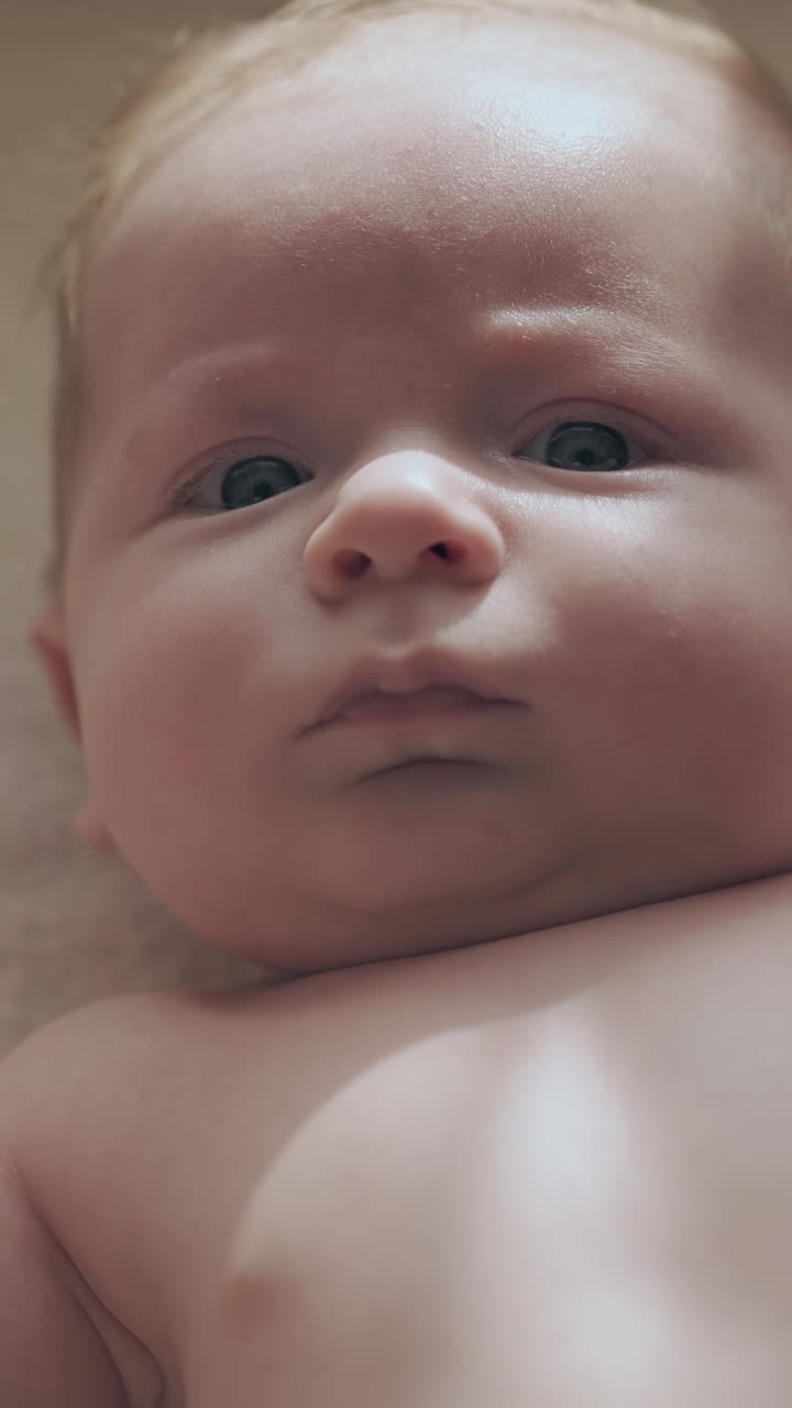 concentrated and serious infant boy with large blue eyes and adorable cheeks lies on changing table extreme close view