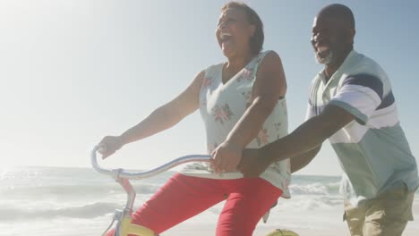 smiling senior african american couple riding bicycles on sunny beach