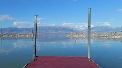 tiro fijo desde el final de un embarcadero de madera roja que mira hacia la entrada del puerto deportivo de saratoga springs con agua plana y montañas cristalinas en el fondo, solo unas pocas nubes en la distancia