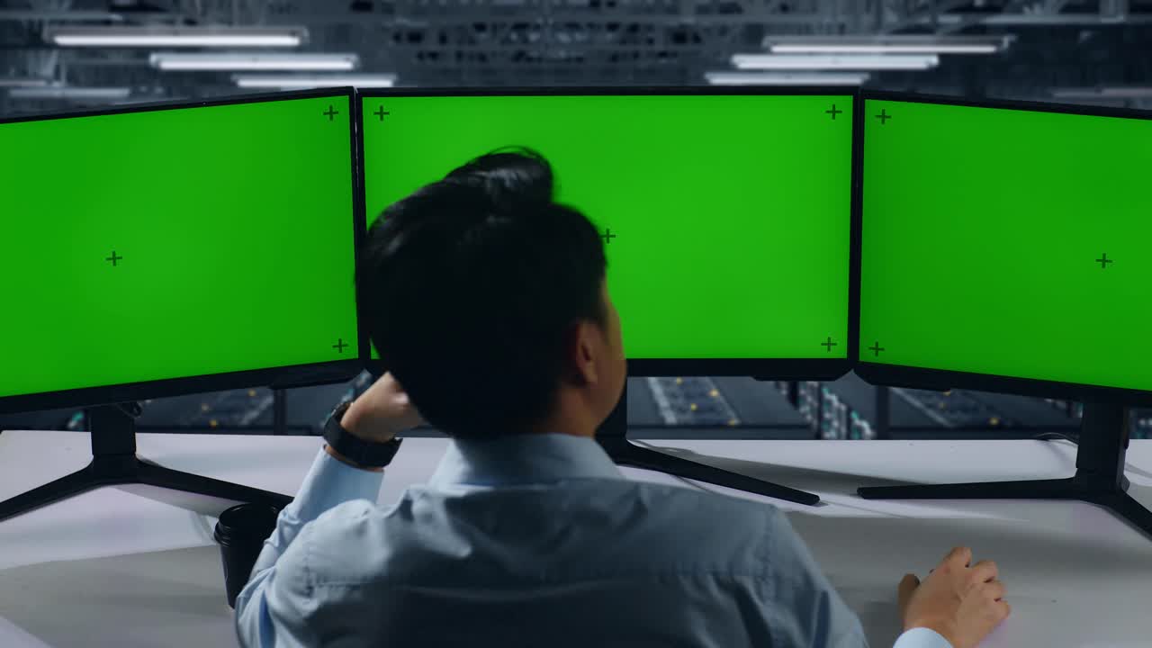 데이터 센터에서 여러 컴퓨터 모니터를 모방하는 지루한 아시아 남자의 뒷면