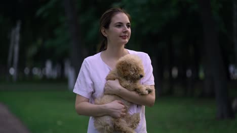 woman with toy poodle walking in a park.