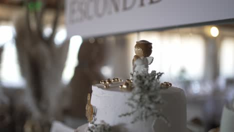 white cake decorated with greenery and a small angel figurine on top