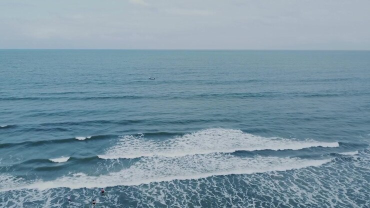 Oceano aperto calmo con onde che si infrangono e una piccola barca in lontananza vicino alla spiaggia di Mompiche, provincia di Esmeraldas, Ecuador, sotto un cielo coperto, ripresa aerea con carrello a sinistra