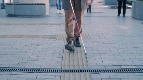 visually impaired man is walking on a tactile warning tile with the help of his cane. detectable warning surface for the vision impaired outdoors in the city.