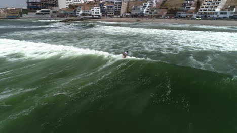 Aerial-view-of-a-people-riding-waves-on-a-coast-of-San-Bartolo,-in-cloudy-Peru