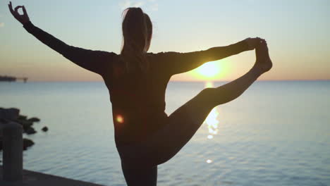 woman getting into balancing yoga pose by the water at sunrise. slow motion