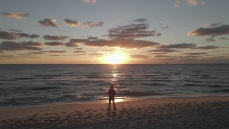 Amanecer-En-La-Playa-Del-Océano-Dorado-Con-Hombre-En-Silueta-Con-Capucha-En-Rayo-De-Sol