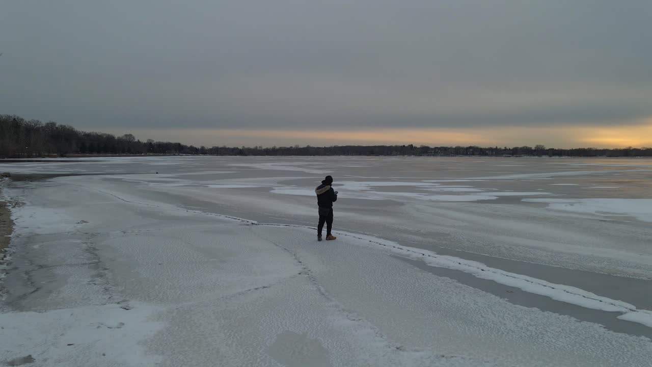 Guy walking on ice, frozen lake surface starring at the sunset, explore Minnesota