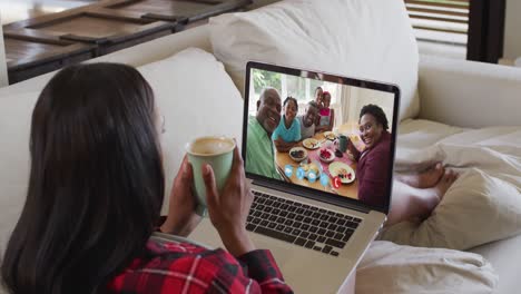 African-american-woman-holding-coffee-cup-having-a-video-call-on-laptop-sitting-on-the-couch-at-home