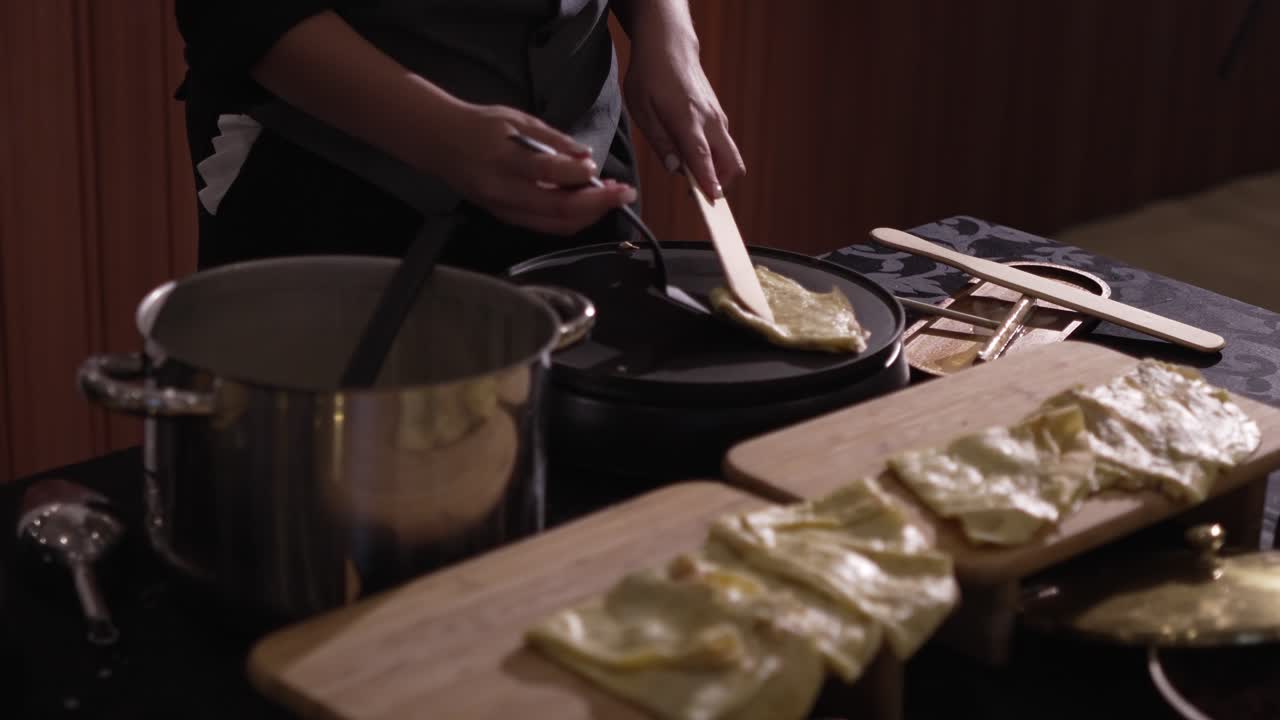 close up of chef preparing traditional crepes or folded pancakes beside hot griddle and pot