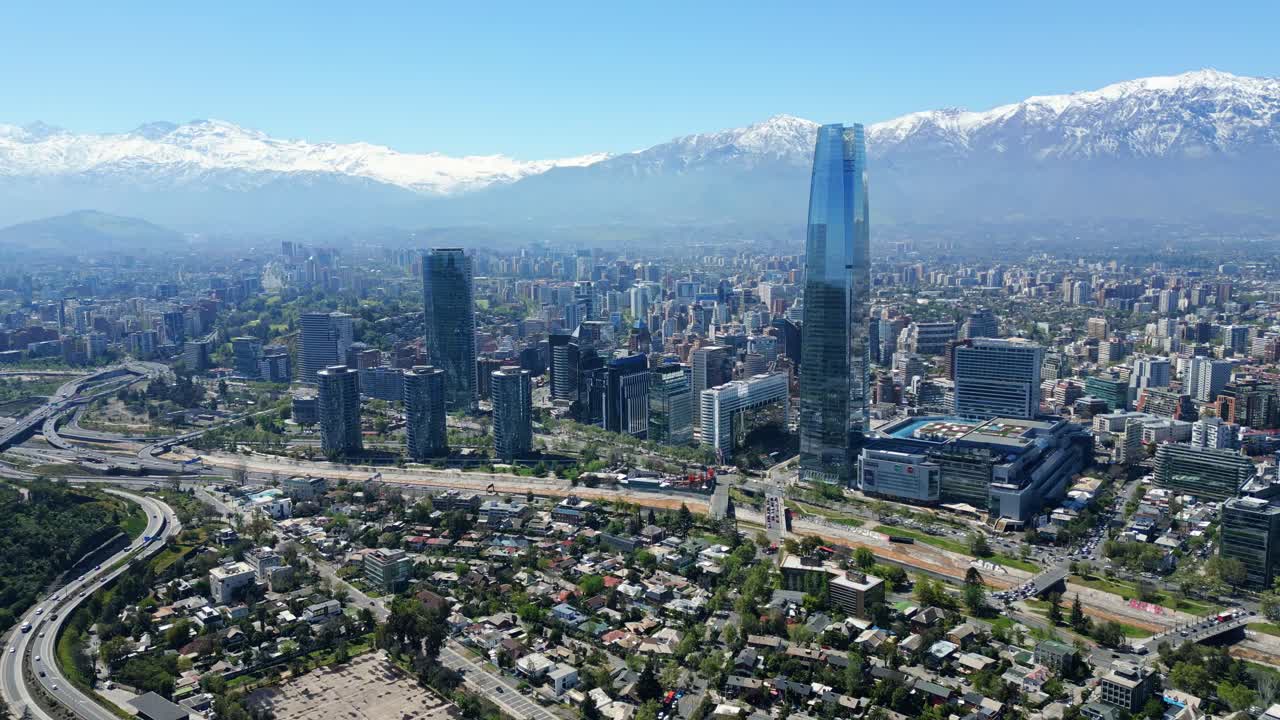Santiago, Chile drone aerial pulling backward over downtown and Costanera Tower with snowcapped Andes in clear daytime
