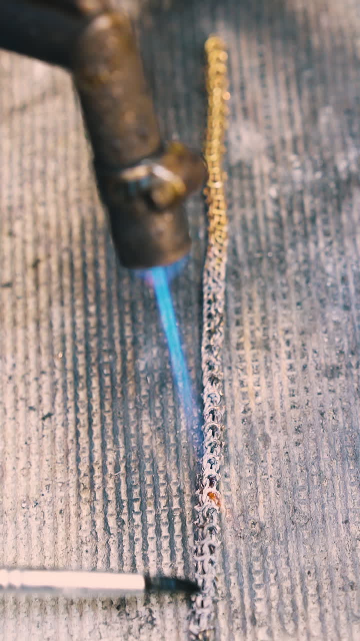 CU: professional jeweler processes long gold chain with heating gas burner and special material on asbestos sheet closeup