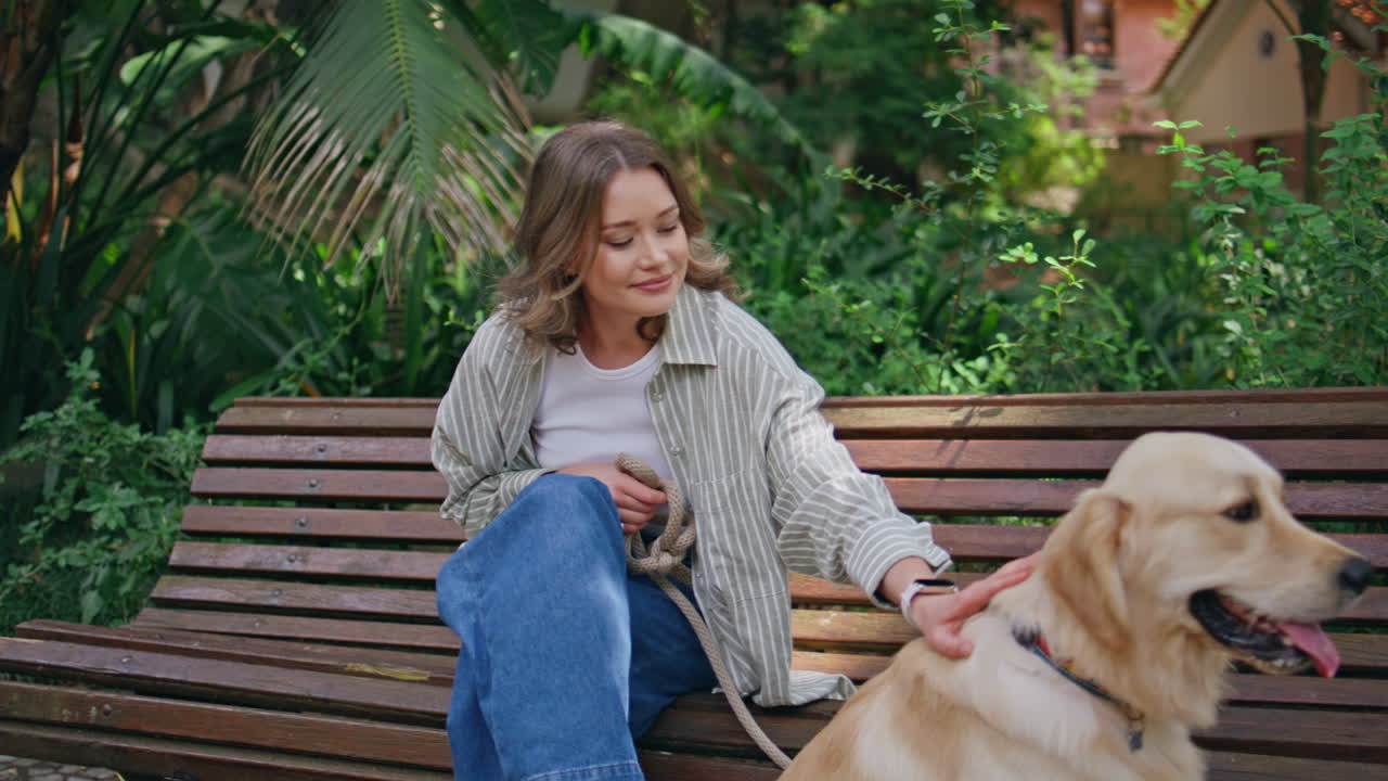 Dog owner sitting bench park with golden retriever closeup. Relaxed girl petting