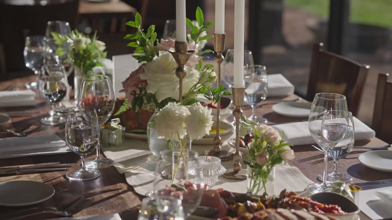 Medium close-up of rustic wooden wedding table with lit candles, empty goblets, plates, napkins, cutlery, and an appetizer being served as part of the elegant decor setup