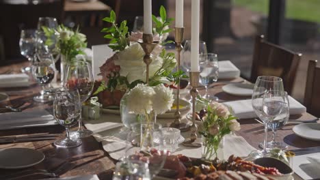 medium close-up of rustic wooden wedding table with lit candles, empty goblets, plates, napkins, cutlery, and an appetizer being served as part of the elegant decor setup