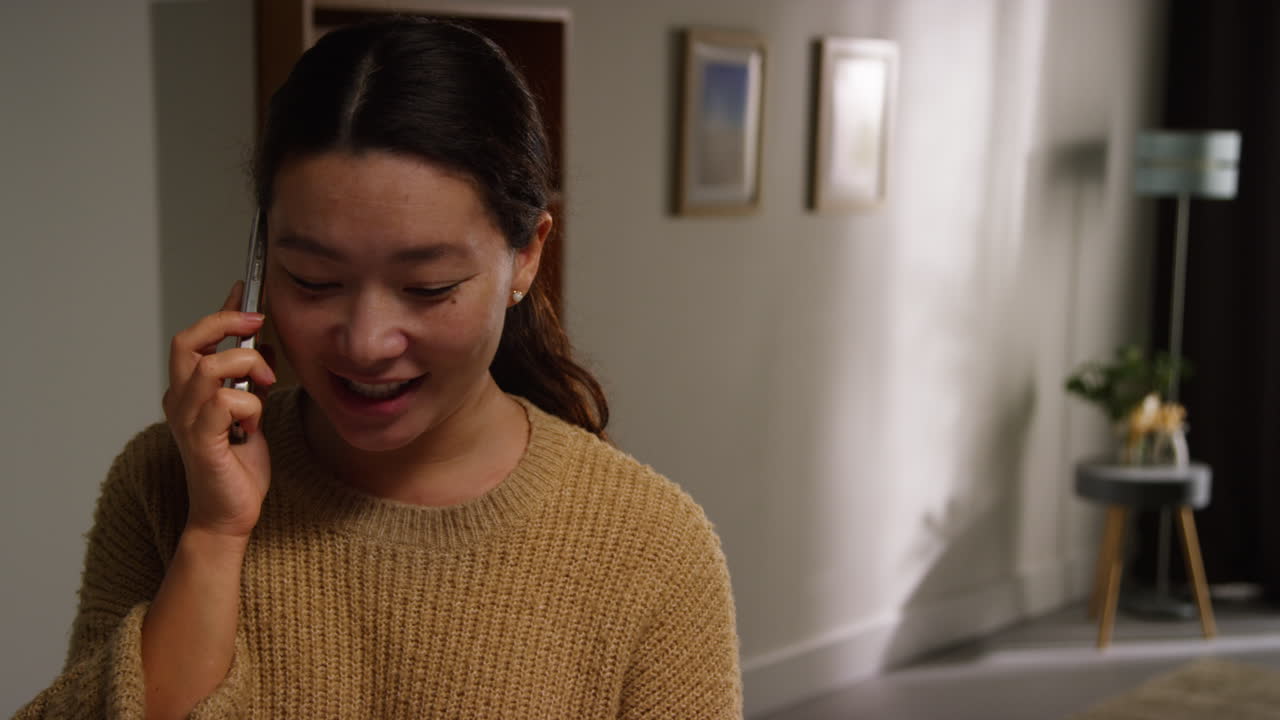 웃고 웃는 여자가 집에서 휴대 전화로 이야기하고 있습니다.