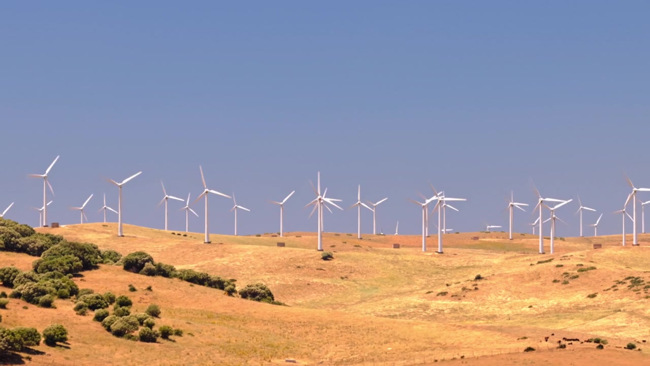 Images cinématographiques par drone d'un grand parc éolien avec des éoliennes générant de l'électricité propre et renouvelable à travers un paysage rural. Infrastructure énergétique durable soutenant la décarbonisation et les objectifs climatiques.