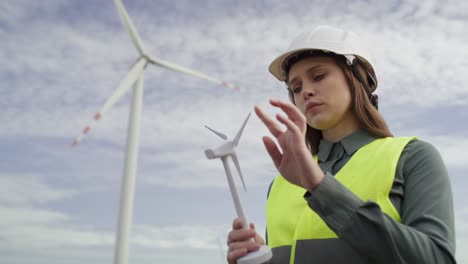 ingeniera caucásica de pie al aire libre y comprobando el modelo de plástico del campo de la turbina eólica.