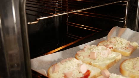 hombre casado con anillo de bodas empujando sándwiches caseros al horno caliente para cocinar