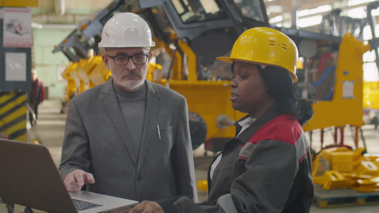 Female Factory Worker and Engineer Using Laptop and Talking