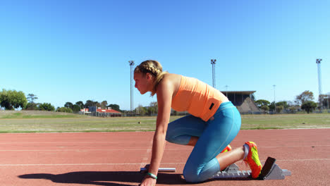 Vista-Lateral-De-Una-Atleta-Caucásica-Tomando-Posición-Inicial-En-Una-Pista-De-Atletismo-En-Un-Recinto-Deportivo-4k