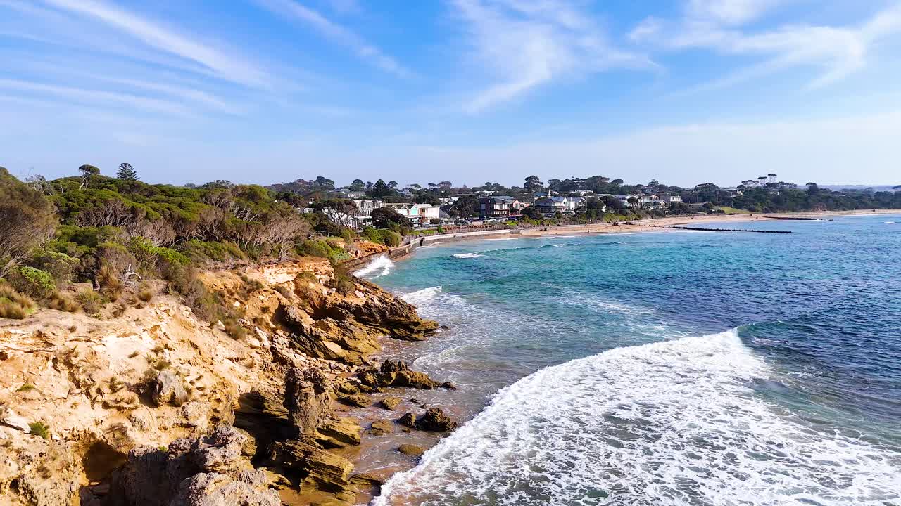 Aerial footage captures Point Lonsdale's rugged coastline, clear waters, and residential area under bright daylight