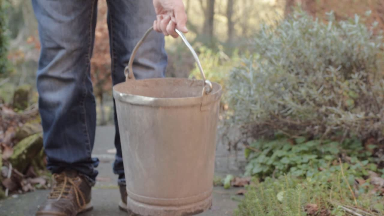 Lady picking up metal bucket on garden pathway