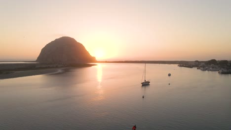 A-sailboat-sails-into-Morro-Bay-California-at-sunset-as-seagulls-fly-over