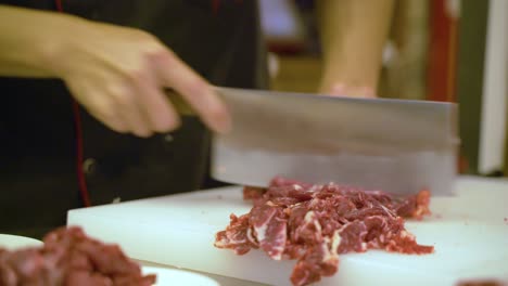 skilled hands of chinese chef cutting raw beef meat, close up