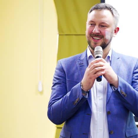 professional coach in white shirt and blue suit speaking into the microphone in conference hall. handsome man speaker conducting a lecture with a smile on his face.