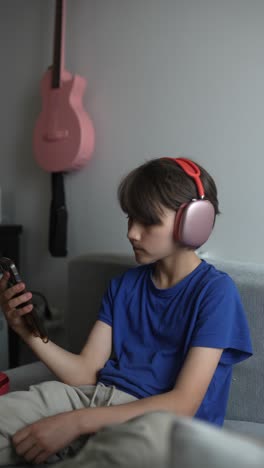 teenage boy listening to music on a smartphone while sitting on a couch