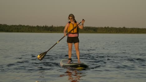 pretty girl paddle boarding into sunset light slomo