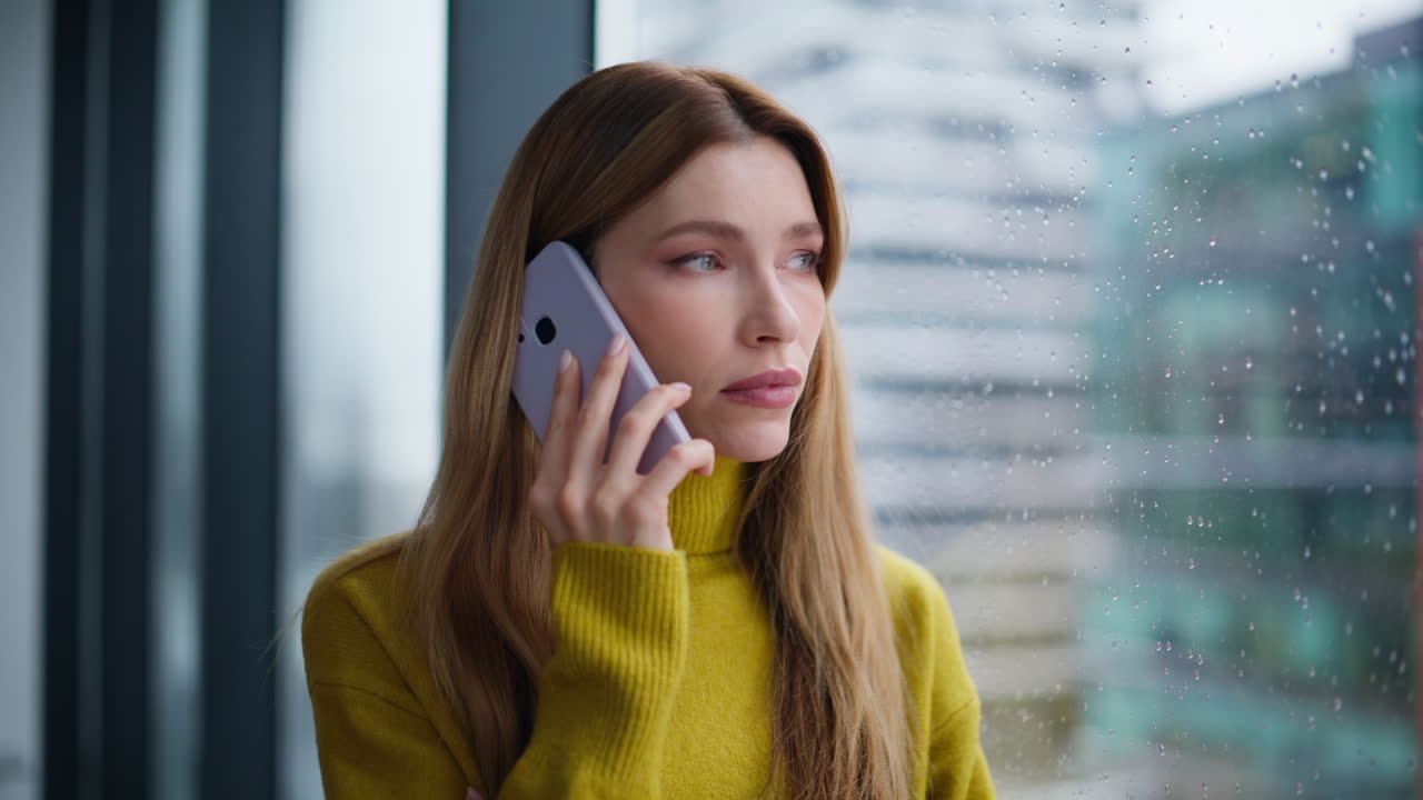 Portrait woman calling mobile phone looking city view through rainy window