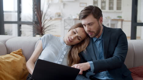 Lächelndes-Paar-Schaut-Im-Wohnzimmer-Auf-Einen-Laptop.-Entspannte-Familie-Redet-Auf-Dem-Sofa.