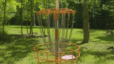 un primer plano de una canasta de golf de disco a medida que el disco entra, destacando el objetivo del juego en un parque boscoso