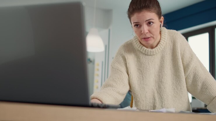 Portrait of woman in startup company office in video call conference on laptop presenting clipboard with financial statistics