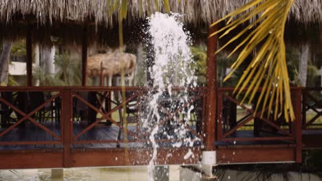 cinematic slowmo of water fountain next to thatched gazebo over water