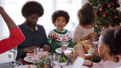 multi generation mixed race family sitting at christmas dinner table wearing paper crowns, panning shot