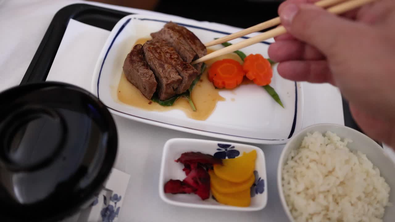 Eating steak, vegetables, and rice with chopsticks